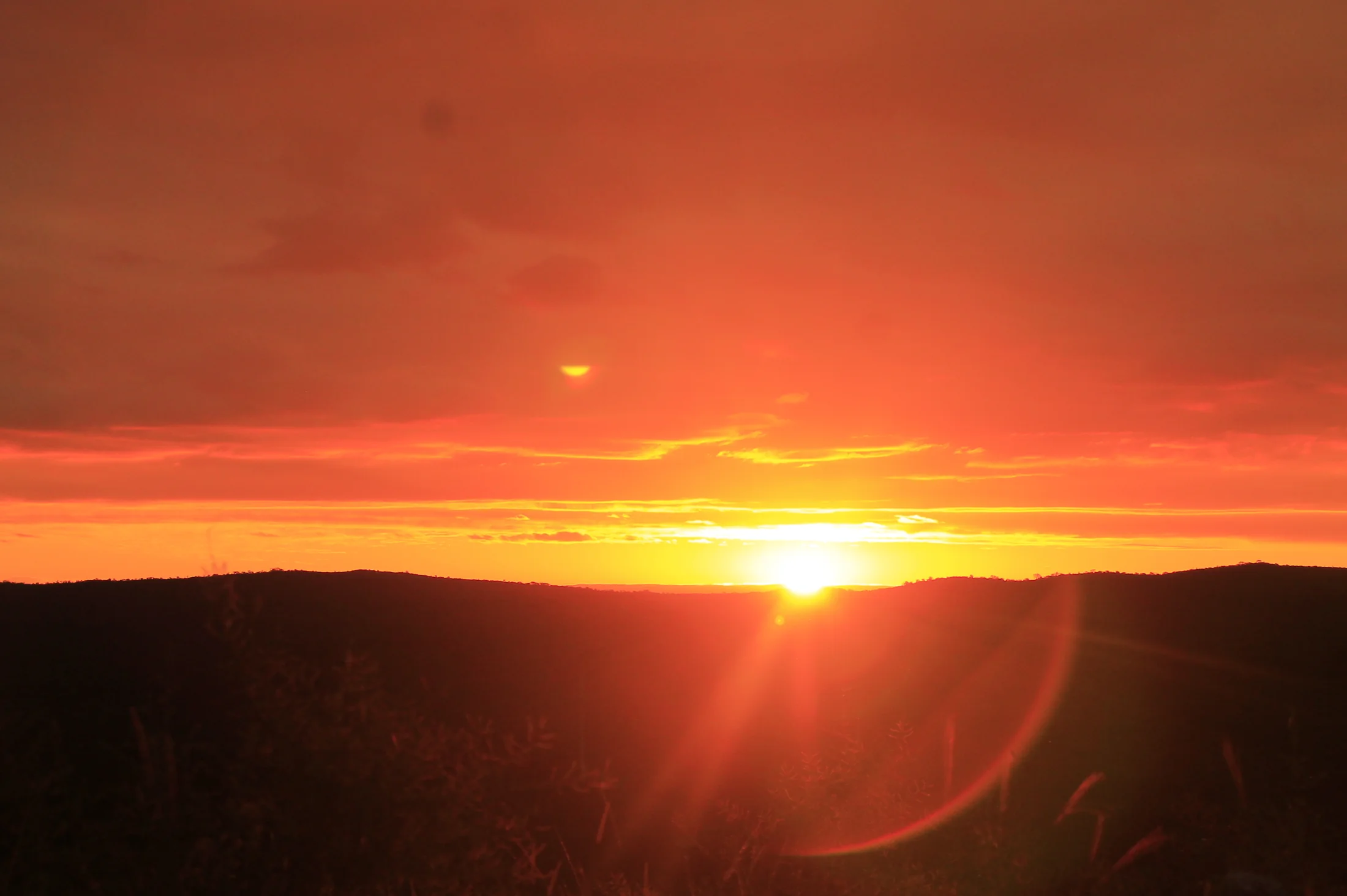 Atardecer de fuego, sol hundiéndose entre cerros oscuros